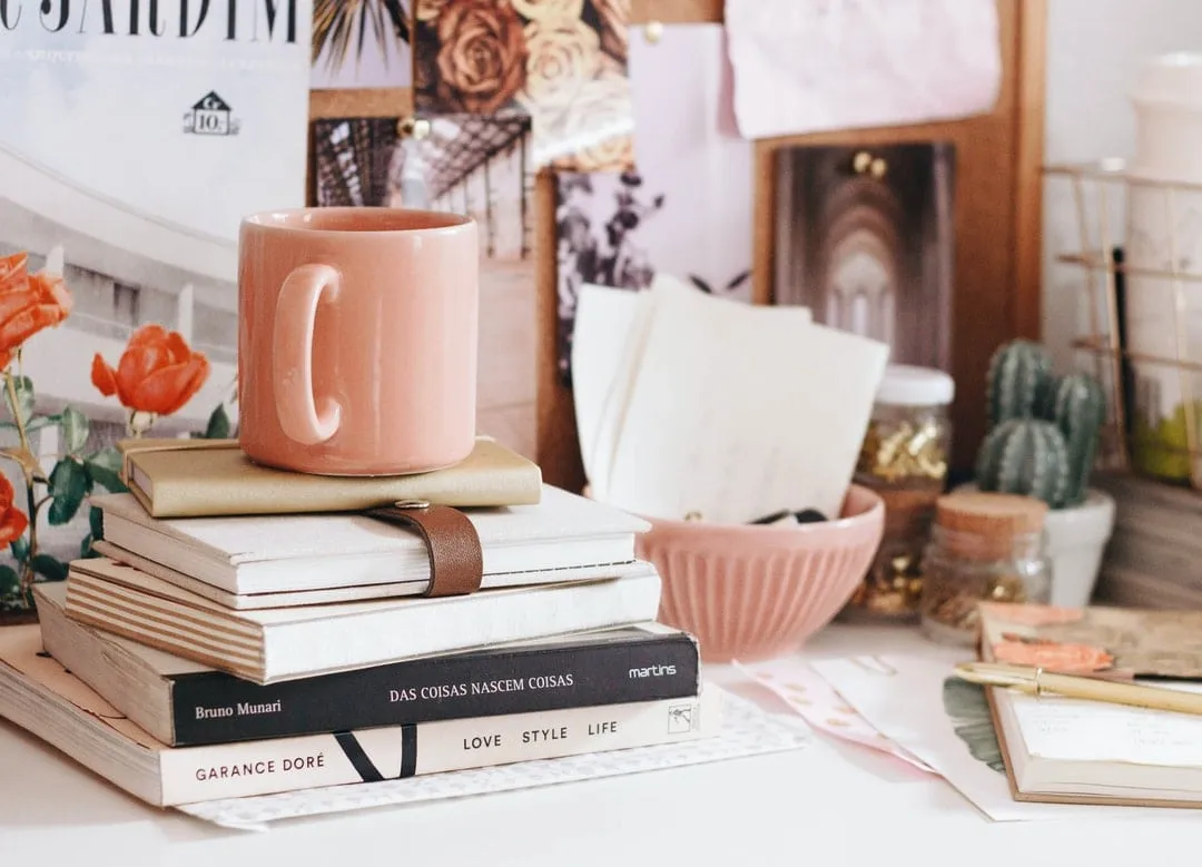 books, notebooks, and a cup on top of a desk
