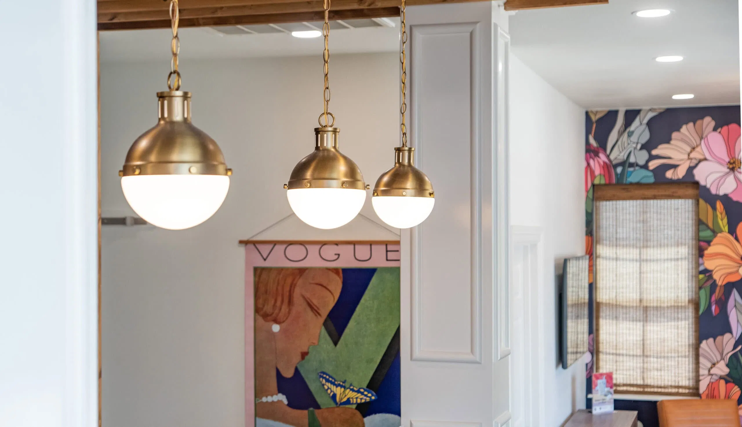 Three spherical pendant lights with brass finishes hang from the ceiling, creating a well-curated look. A colorful art piece featuring a profile of a woman and the word 