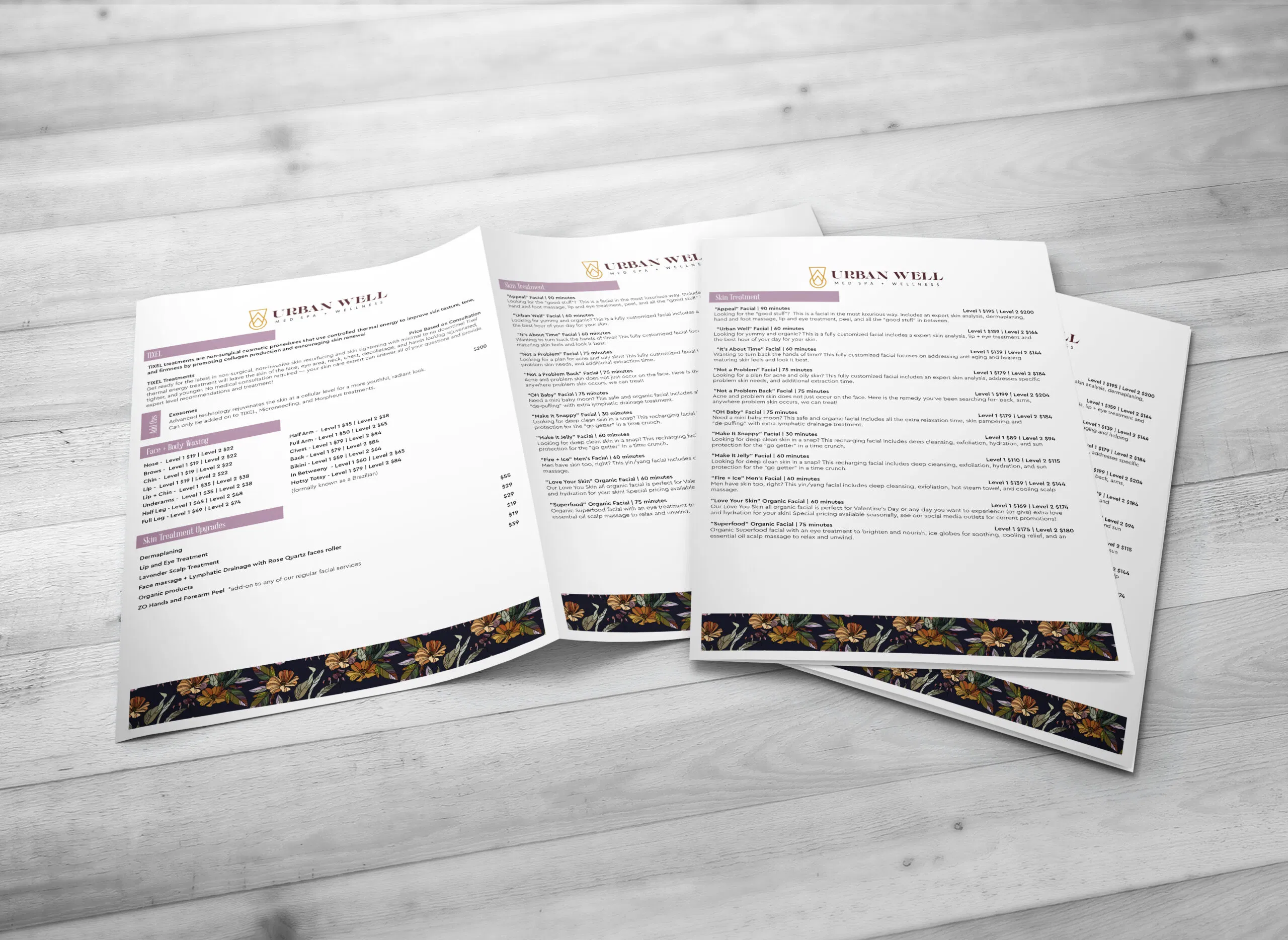 Three white menus with floral borders at the bottom are displayed on a light wooden surface. The menus are titled 