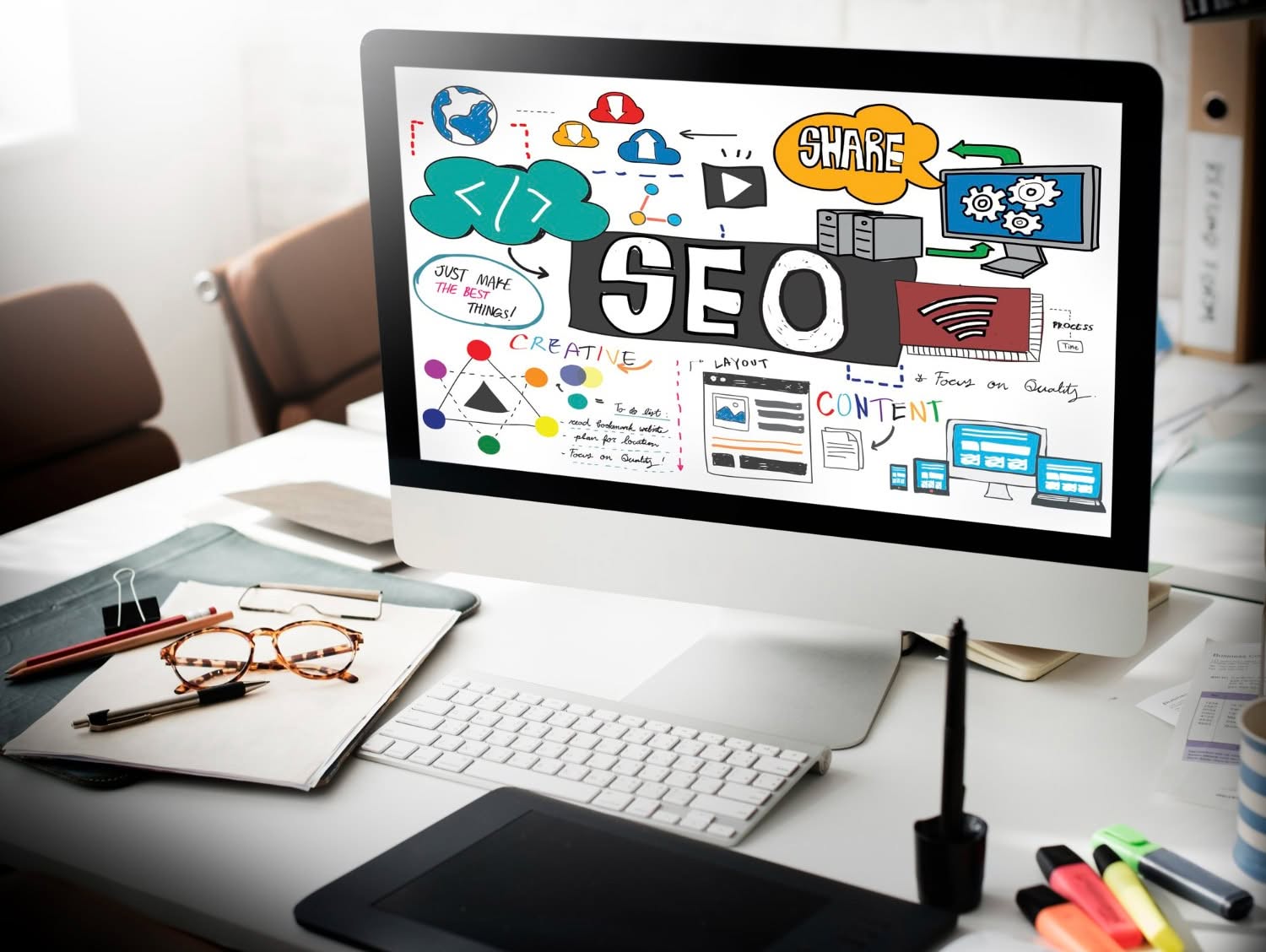 A computer monitor displaying a colorful SEO infographic, surrounded by office items including glasses, a notebook, a pen, and a graphics tablet on a white desk—ideal inspiration for agencies focused on content marketing. - Market Design Team: Define. Structure. Expand.