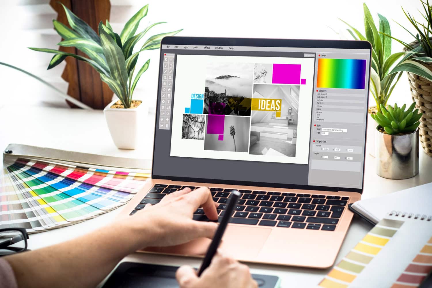A person in Angleton uses a stylus and laptop to work on a graphic design project, with color swatches, plants, and a coffee cup on the white desk. The screen displays various design elements and images for the best creative workflow. - Market Design Team: Define. Structure. Expand.